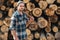 Strong bearded woodcutter wearing plaid shirt hold axe in hand on background of sawmill