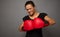 Strong concentrated African woman looks at camera posing against gray wall background with red boxing gloves. Concept of Black