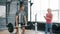 Strong guy lifting barbell training with weight-lifting indoors in gym working with woman coach