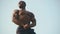 Strong handsome african american bodybuilder with naked torso showing his perfect muscles on the clear blue sky