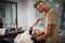 A strong handsome man getting shaved by a professional barber in a barbershop on a light blurred background.