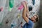 Strong healthy active handsome man with beard wearing trendy glasses climbing on wall with color holds during training workout