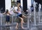 Strong heat in the city: woman and little girl playing with fountain water jets at the square