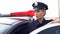 Strong lady in police uniform standing near patrol car, protecting law and order