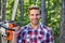 Strong lumberjack with chainsaw in a plaid shirt. Lumberjack worker walking in the forest with chainsaw. Woodcutter with