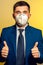 Strong man, businessman in tie and medical mask demonstrates confidence at work in pandemic coronavirus. Shows a thumbs-up of both