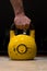 Strong man hand holding old and used big yellow kettlebell on a wooden floor in a gym