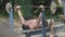 Strong man raising the barbell lying on the bench in the park. Exercise for biceps. Keeping body in shape. Fitness