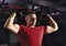 Strong man  showing his biceps arm in red t-shirt and sporty gloves on dark sport fitness club background. Closeup