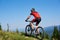 Strong man tourist cyclist in helmet, sunglasses and full equipment riding bike on grassy hill.