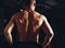 Strong masculine shirtless man athlete standing in dark fitness club background. Closeup portrait with empty copy space. Back view