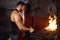 Strong muscular blacksmith prepares iron on fire