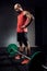 Strong muscular bodybuilder athletic man preparing for training with barbell on dark studio