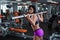 A strong, muscular dark-haired girl performs squats with barbell. Gym