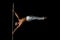 A strong muscular guy dressed in white pants performs a trick on a pole in on a black background