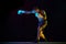Strong, muscular young man, boxing athlete in gloves, training, fighting isolated over black background in neon light
