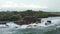 Strong ocean waves crashing into rocky cliff with Tanah Lot temple in Bali, Indonesia. Aerial shot circling famous