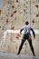 Strong rock-climber without forearm, standing in front of high artificial climbing wall