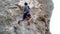 strong and skillful man climber climbs on vertical cliff by tough route, clippes rope to carabiner, makes several wide