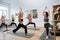 Strong spirited women practice yoga in front of instructor, holding warrior pose