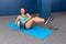 Strong and sporty fitness woman in sportswear pumping a press with heavy medicine ball on blue yoga mat at gym