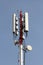 Strong tall red and white metal pole with multiple cell phone transmitters and antennas mounted on each side with clear blue sky