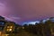 Strong thunderbolt in purple stormy sky over modern houses at night