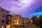 Strong thunderbolt in purple stormy sky over modern houses at night