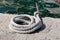 Strong white heavily used rope left on edge of stone pier next to calm sea with oily reflection