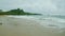 strong white waves of blue ocean run on golden sandy beach against cloudy sky