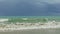 Strong white waves of blue sea slowly running to sandy beach against stormy sky