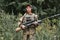 strong woman in military gear and bulletproof vest stands in field of forest