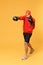 Strong young bearded fitness guy boxer sportsman in hat, hoodie, shorts in home gym isolated on yellow background