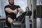 Strong young man with beard in black sportswear pulling heavy weight sitting in exercise equipment during hard workout in sport