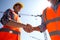 Structural engineer and architect dressed in orange work vests and helmets shake hands on the building site near the