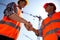 Structural engineer and architect dressed in orange work vests and helmets shake hands on the building site near the