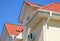 A stucco house with a red metal roof, attic and air conditioner outdoor unit with a close-up on a white roof soffit board and rain