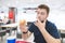 Student with a beard sits with a bright fast food restaurant with a burger in his hands and lickes his fingers