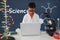 Student boy at table using a computer against blue blackboard with science text and graphics