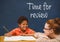 Student boy and teacher at table against blue blackboard with time for review text