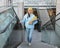 A student with bright folders in her hands climbs the stairs and smiles at the camera, photo from the top angle.