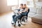 Student with disability sitting on wheelchair. Cheerful woman stand behind and embrace him. Looking on laptop. Young man