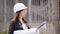 Student girl in protective helmet and goggles and inspects the construction site, using the technical documentation