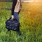 Student girl walking and carrying black leather laptop case bag outdoors on sunny green grass meadow