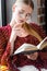 Student in glasses and blouse reading book in apartment