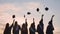 Student graduates toss their caps at sunset.