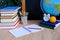 Student home office table with white alarm clock, books, orange, colored notebooks, pencils in glass, chalk board, globe, white