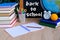 Student home office table with white alarm clock, books, orange, colored notebooks, pencils in glass, chalk board, globe, white