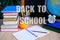 Student home office table with white alarm clock, books, orange, colored notebooks, pencils in glass, chalk board, globe, white