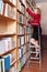 Student is looking books on the shelves standing on a ladder